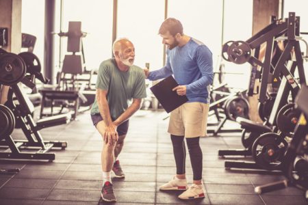 Stretching legs. Personal trainer giving support senior man at gym.